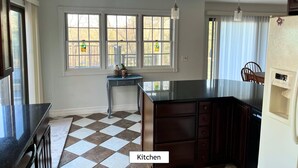A kitchen with a checkered floor, a dining area with a table and chairs, and large windows with curtains. - Spacious House for Beach Getaway - Outdoor Shower -Beach Pass Included! (Charlestown)