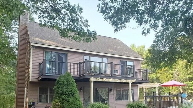 A two-story house with a balcony, a covered porch, and a small deck with a red umbrella. - Spacious House for Beach Getaway - Outdoor Shower -Beach Pass Included! (Charlestown)