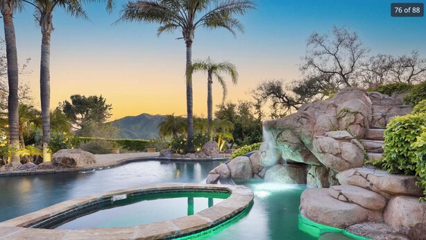 A swimming pool with a waterfall feature, surrounded by rocks and palm trees. - Spectacular Mountain & Vineyard View Estate in the Malibu Wine Trail (Malibu)