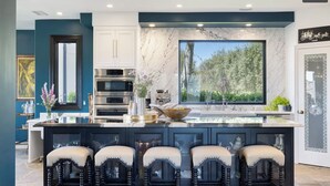A modern kitchen with a large island, bar stools, and a view of the outdoors. - Spectacular Mountain & Vineyard View Estate in the Malibu Wine Trail (Malibu)