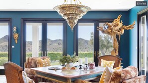 A dining area with a table set for four, surrounded by wicker chairs, a chandelier, and a view of a mountainous landscape through large windows. - Spectacular Mountain & Vineyard View Estate in the Malibu Wine Trail (Malibu)
