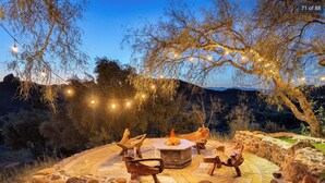 An outdoor seating area with stone walls, a fire pit, and string lights. - Spectacular Mountain & Vineyard View Estate in the Malibu Wine Trail (Malibu)