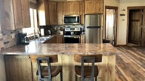 Una cocina con armarios de madera, encimera de granito, electrodomésticos de acero inoxidable y un taburete de bar.