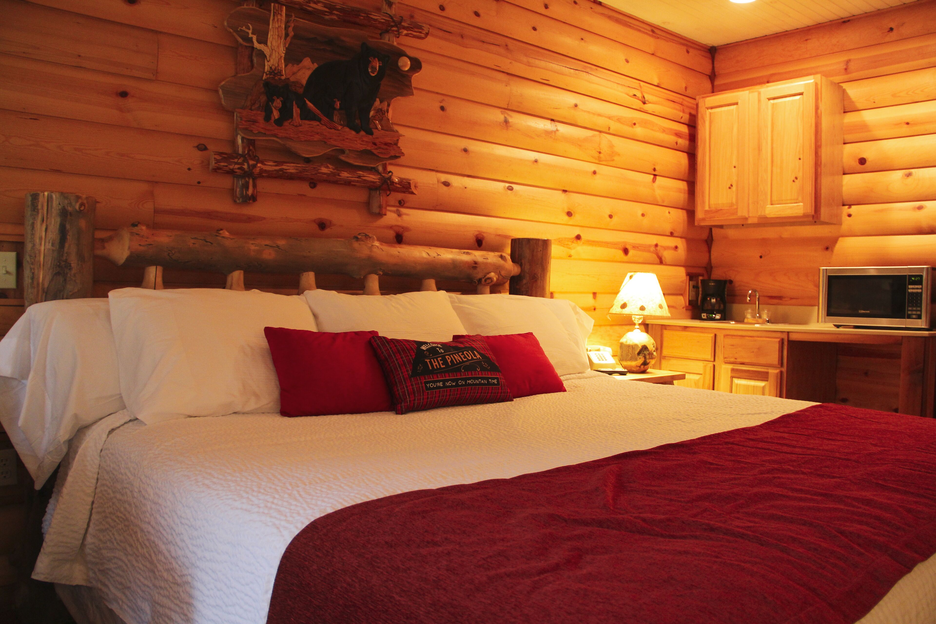 A wooden cabin-style room with a bed, a lamp, a microwave, and a cabinet.