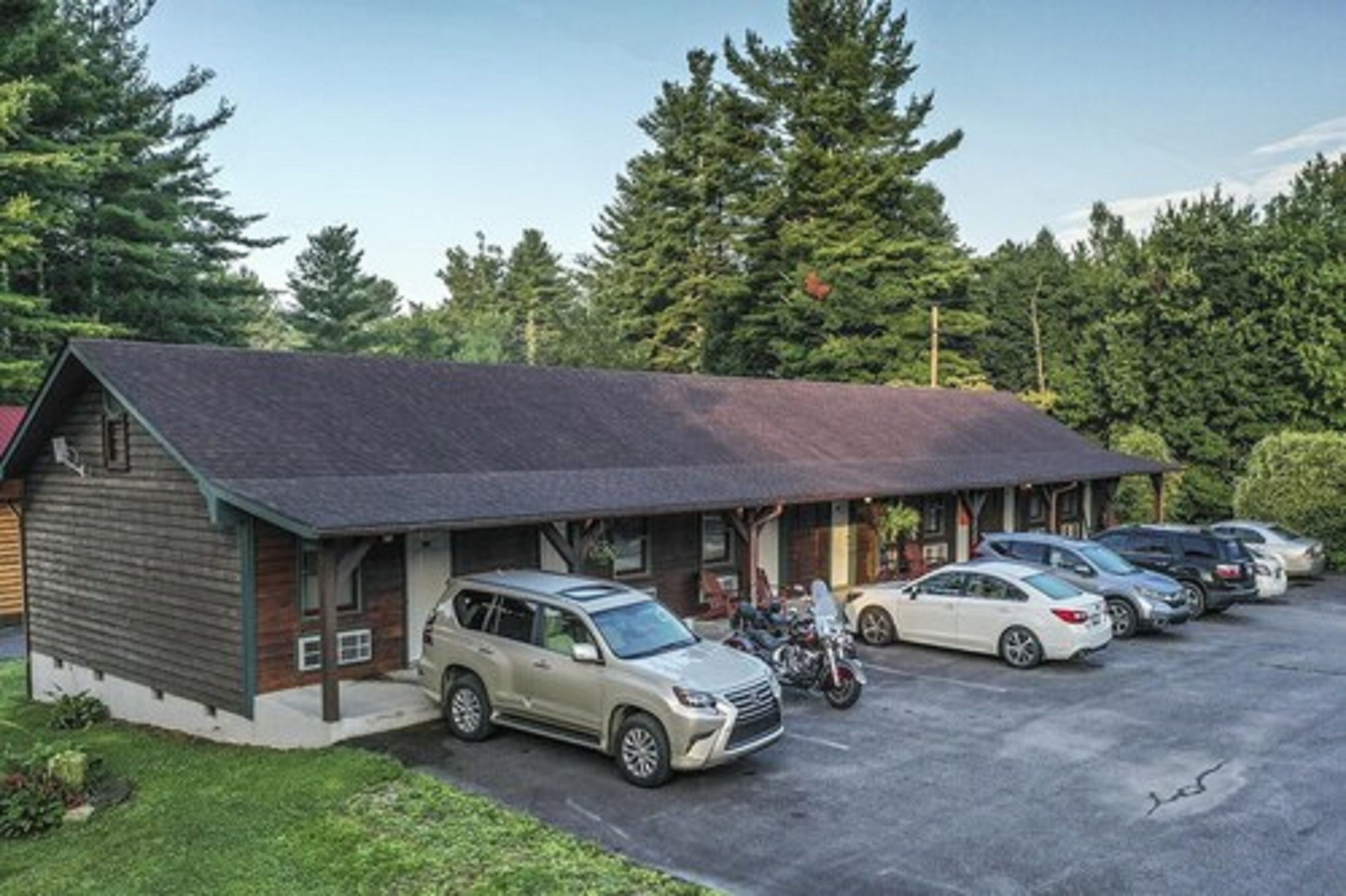 A lodge with a covered parking area, a building with a sloped roof, and a forested backdrop.