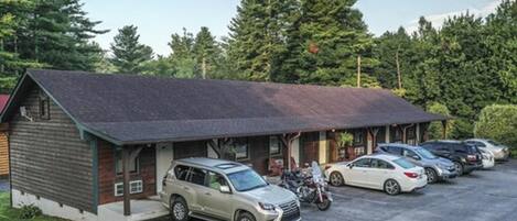 A lodge with a covered parking area, a building with a sloped roof, and a forested backdrop.