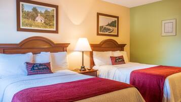 A hotel room with two beds, a nightstand with a lamp, and two framed pictures on the wall.
