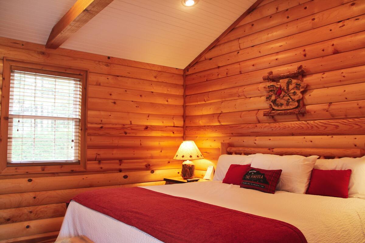 Quarto de cabana de madeira com cama, janela e abajur.