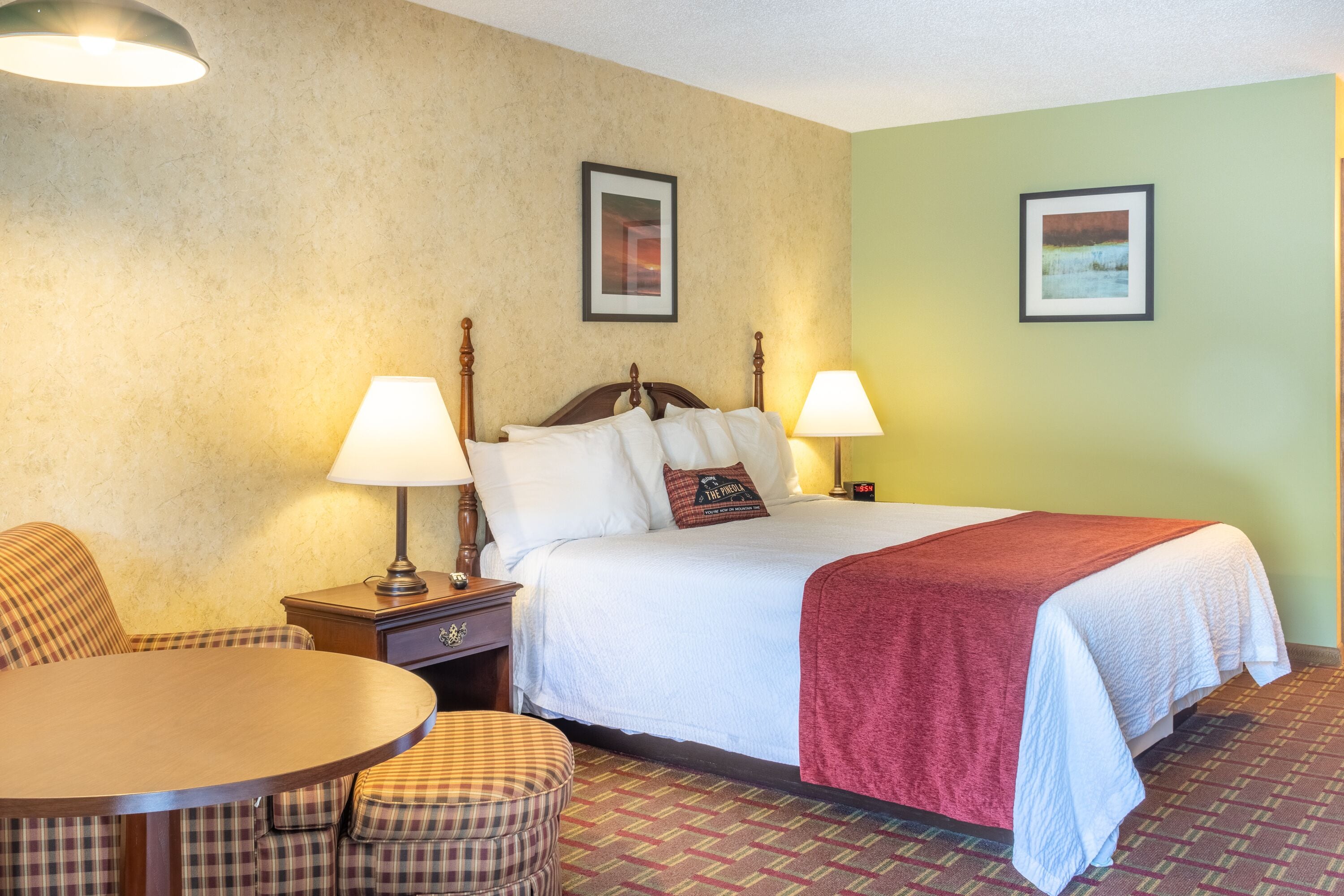 A hotel room with a bed, two bedside lamps, a table, and a chair.