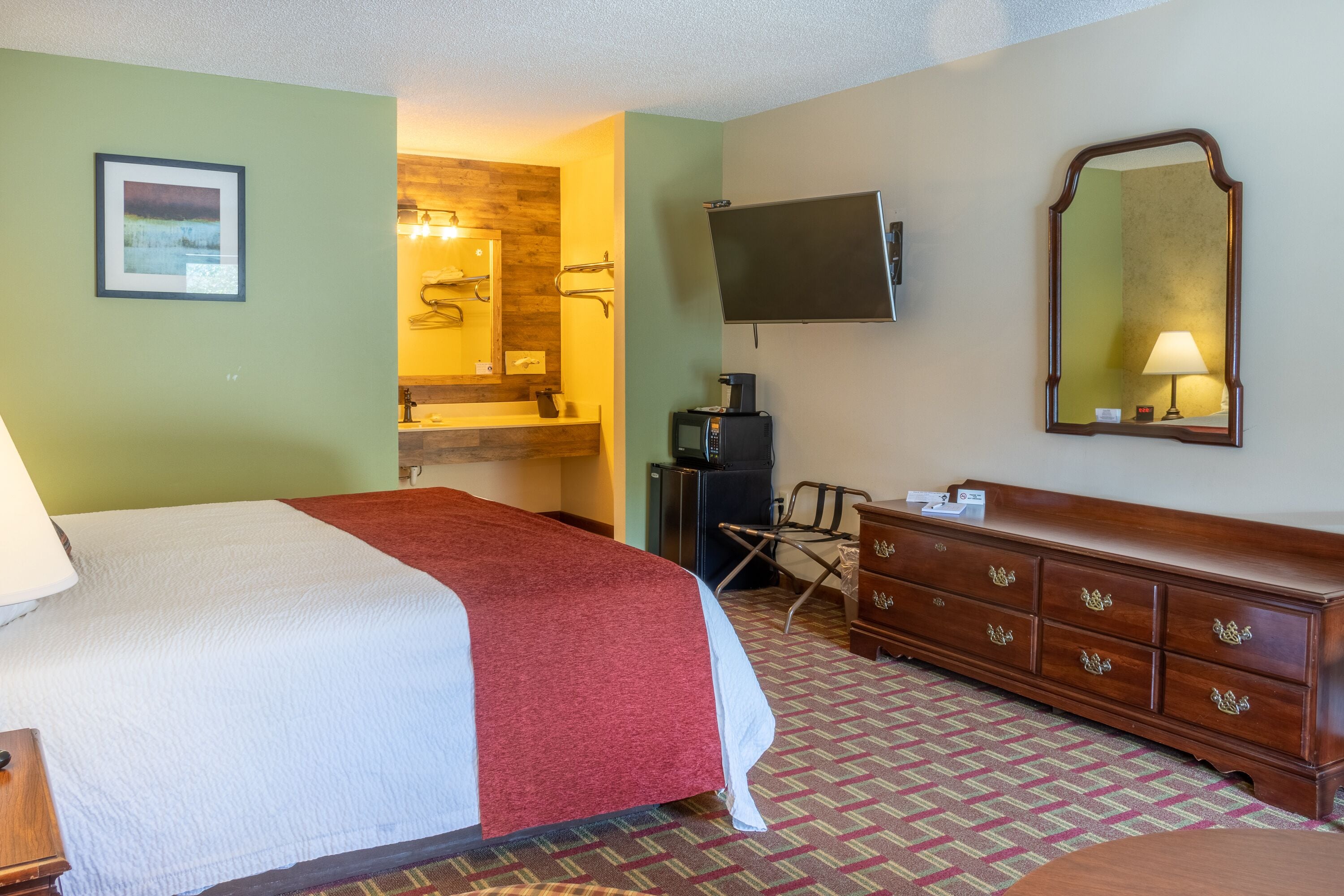 Una habitación de hotel con una cama, un tocador, un televisor y un baño visible a través de una puerta abierta.