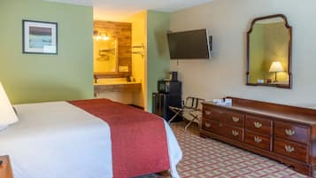 Una habitación de hotel con una cama, un tocador, un televisor y un baño visible a través de una puerta abierta.