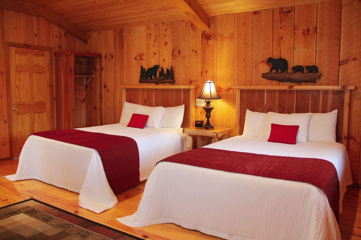 Quarto de cabana de madeira com duas camas, teto de madeira e decoração com tema de urso na parede.