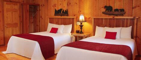 A wooden cabin room with two beds, a wooden ceiling, and a bear-themed decoration on the wall.