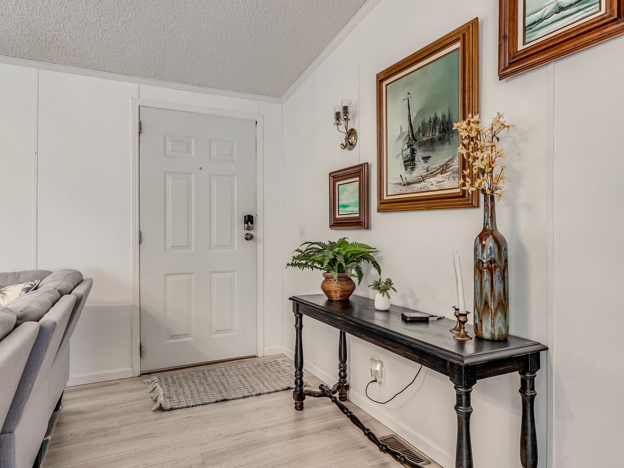 A room with a grey sofa, a black console table with decorative items, a white door, and framed artwork on the wall.