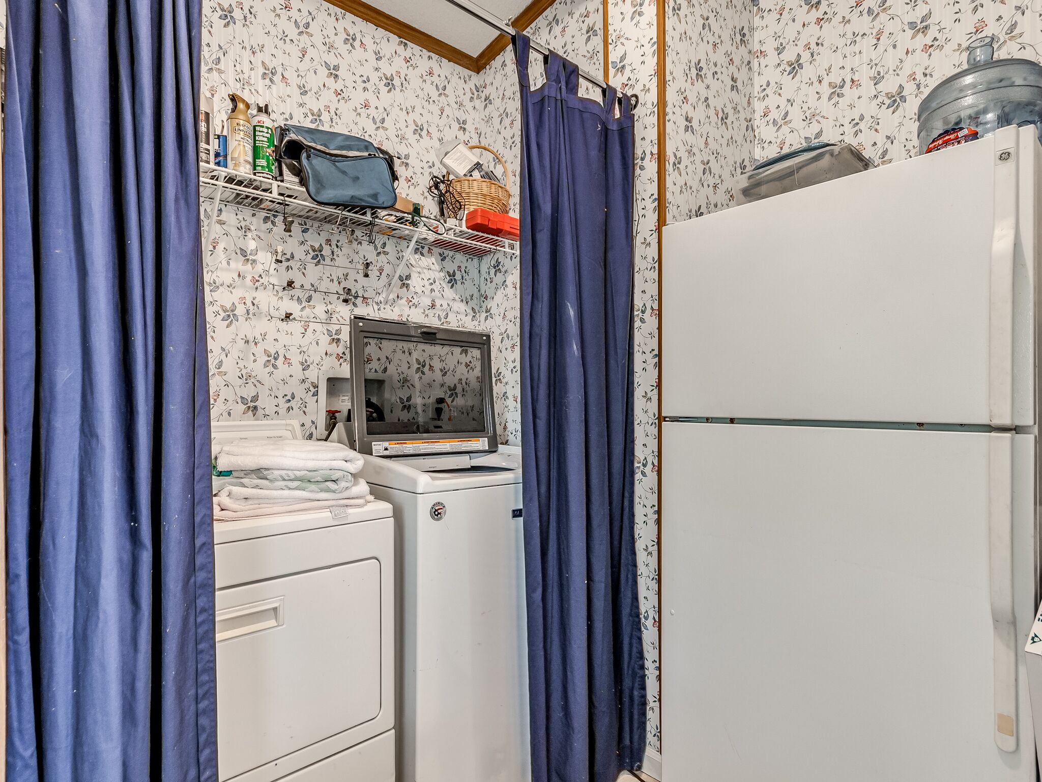 A laundry area with a washing machine, dryer, and shelves above containing various items.