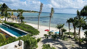 A beachside resort with a swimming pool, palm trees, and a pier extending into the ocean.