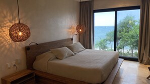 A bedroom with a large bed, two wall-mounted lamps, a ceiling fan, and a view of the ocean.