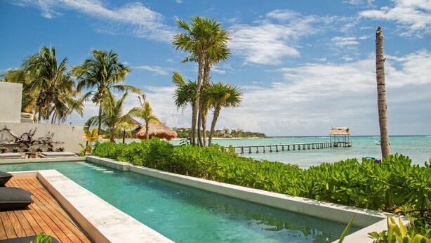 A pool area with a wooden deck, palm trees, and a view of the ocean.