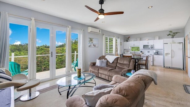 A spacious living area with a balcony, a ceiling fan, and a kitchen with white cabinets. - Soak up breathtaking sunsets from any of our three private balconies!
 (Rincon)