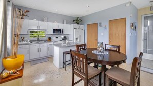 A modern kitchen with white cabinets, a central island, and a dining area with wooden chairs. - Soak up breathtaking sunsets from any of our three private balconies!
 (Rincon)