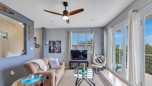 A modern living room with a sofa, a glass coffee table, a ceiling fan, and a large window with curtains. - Soak up breathtaking sunsets from any of our three private balconies!
 (Rincon)