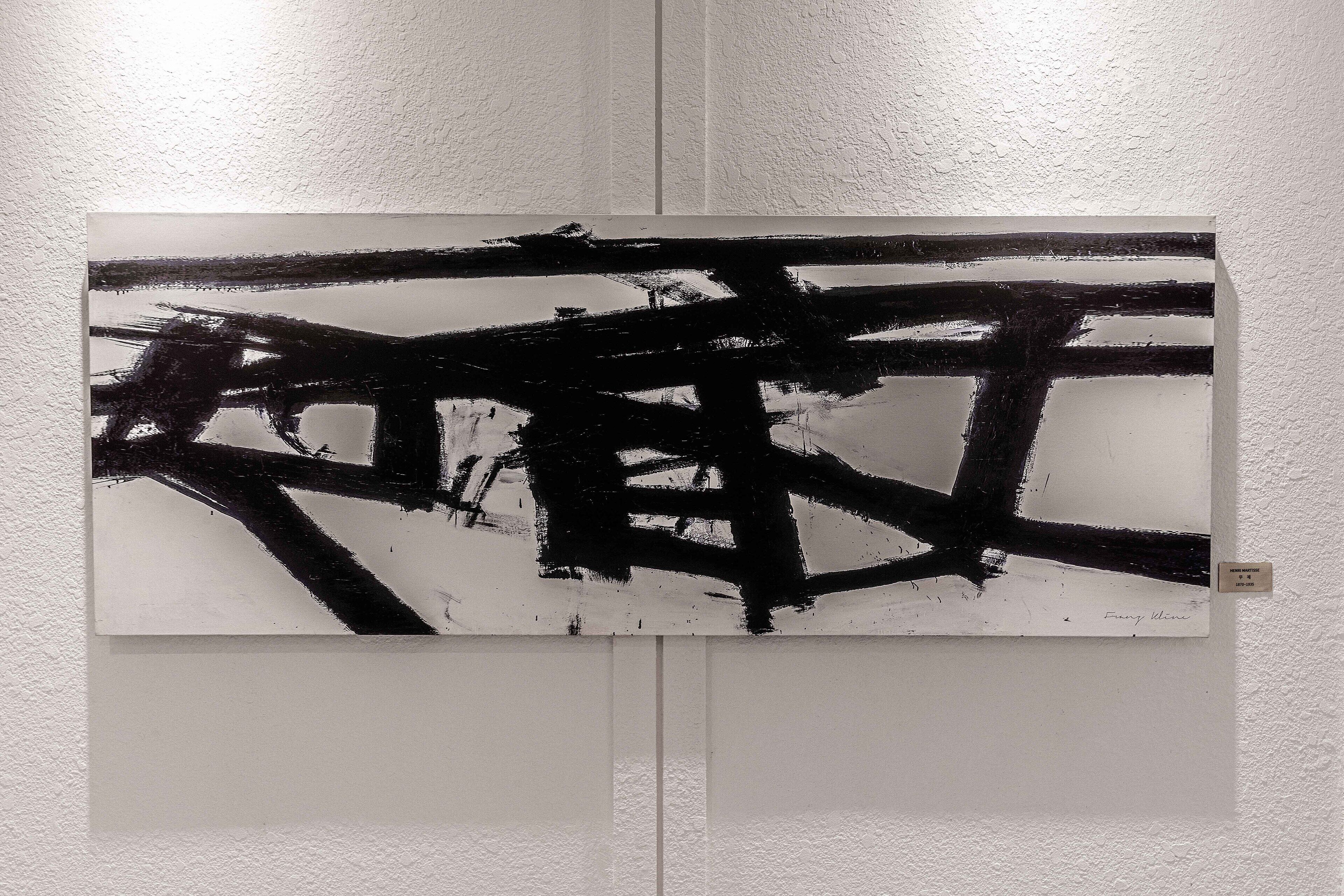 Een schilderij met abstracte zwart-wit strepen op een witte muur.