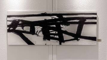 A painting with abstract black and white strokes on a white wall.