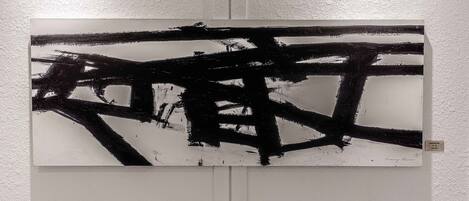 Een schilderij met abstracte zwart-wit strepen op een witte muur.