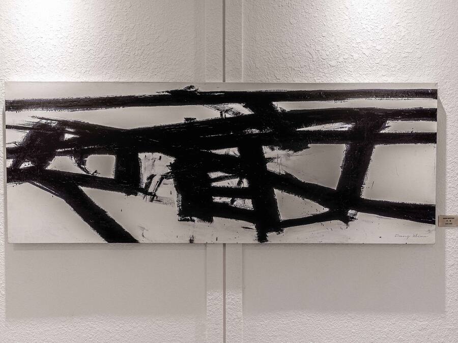 A painting with abstract black and white strokes on a white wall.