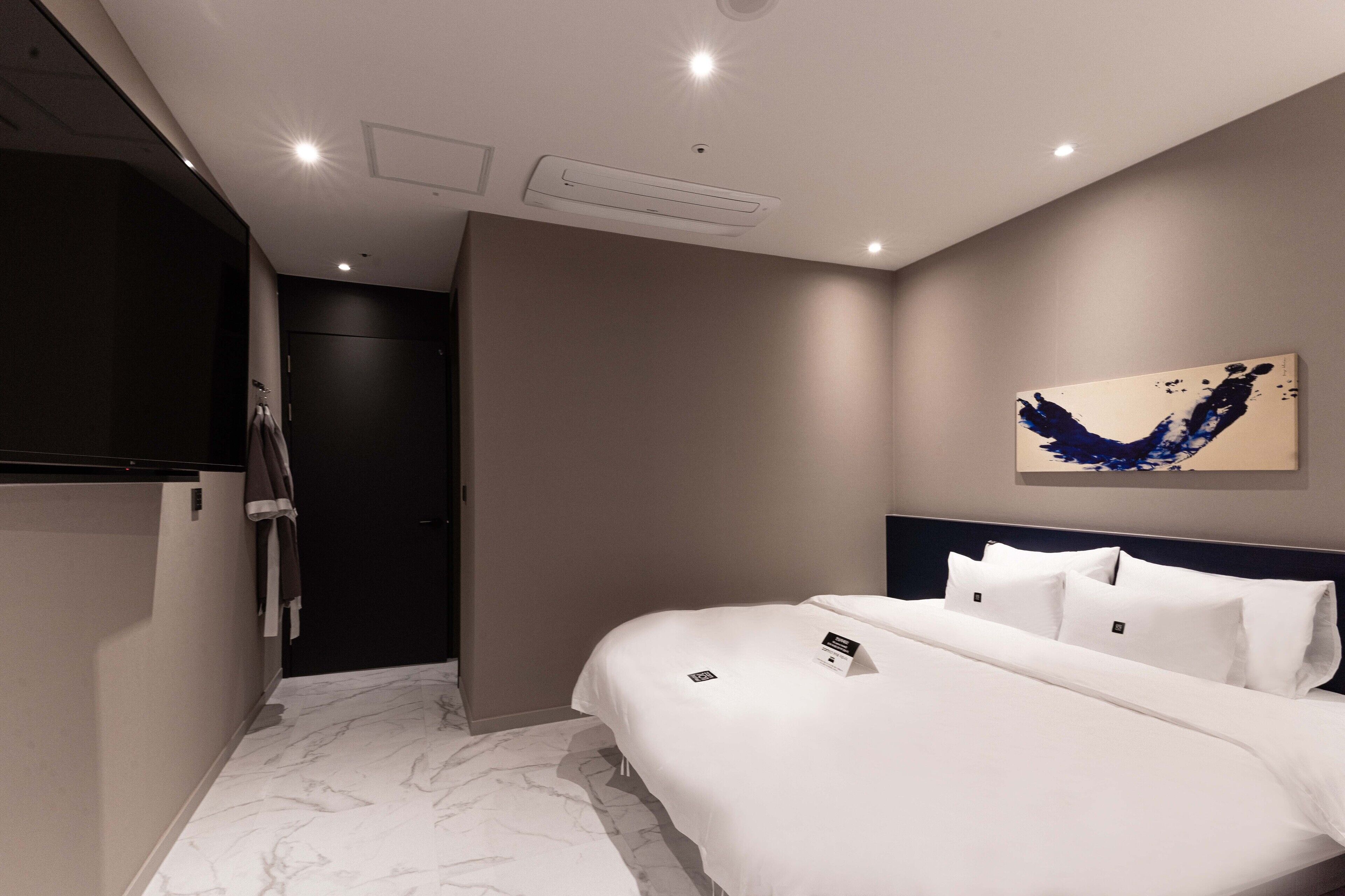 Een moderne hotelkamer met een groot bed, een donkere kast, een schilderij aan de muur en een marmeren vloer.