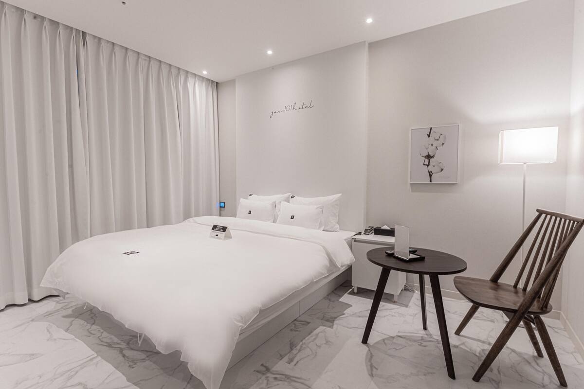 A modern hotel room with a large bed, a bedside table, a chair, and a wall-mounted artwork.