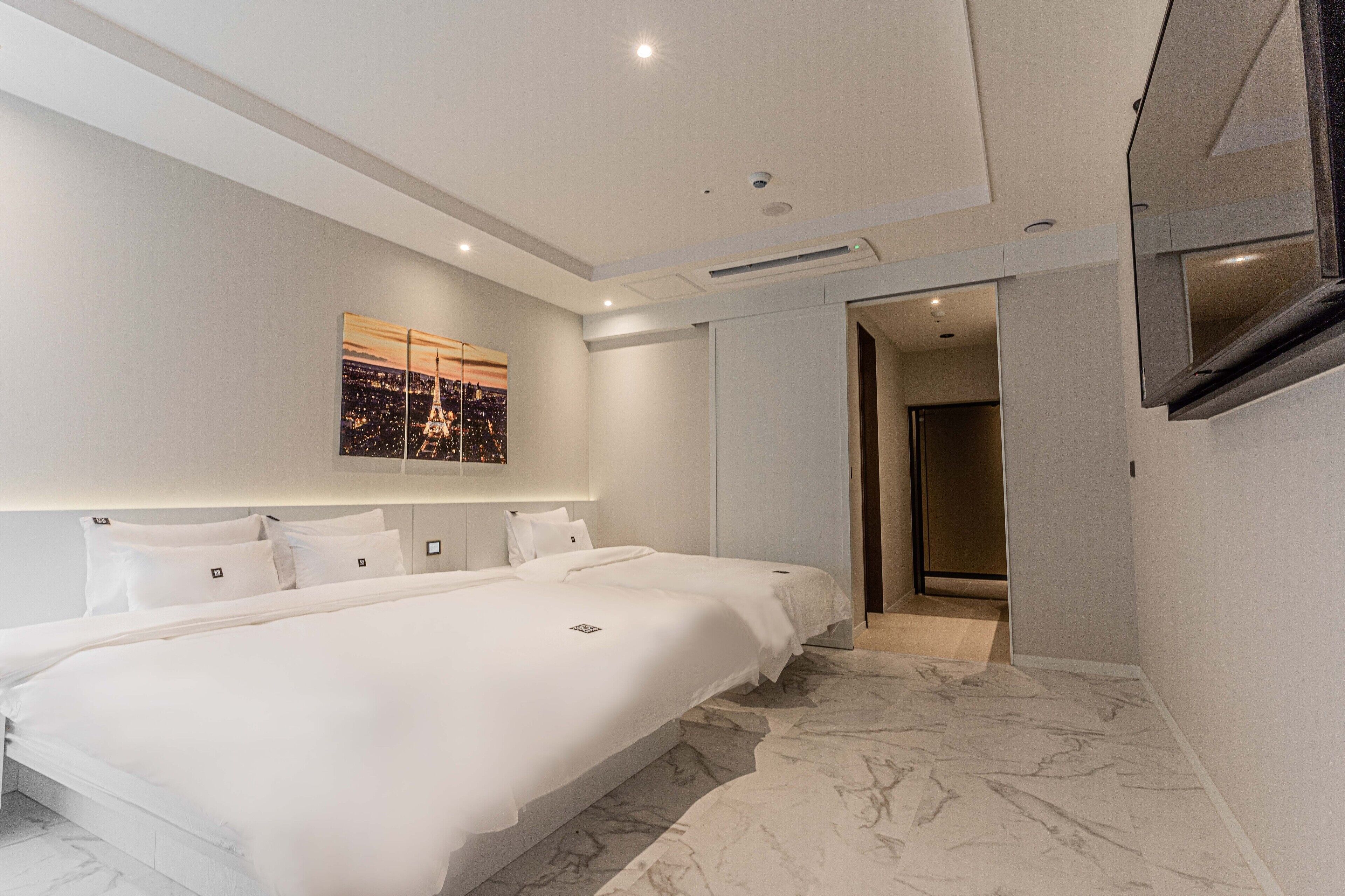 A modern hotel room with a large bed, a flat-screen TV, and a cityscape artwork on the wall.