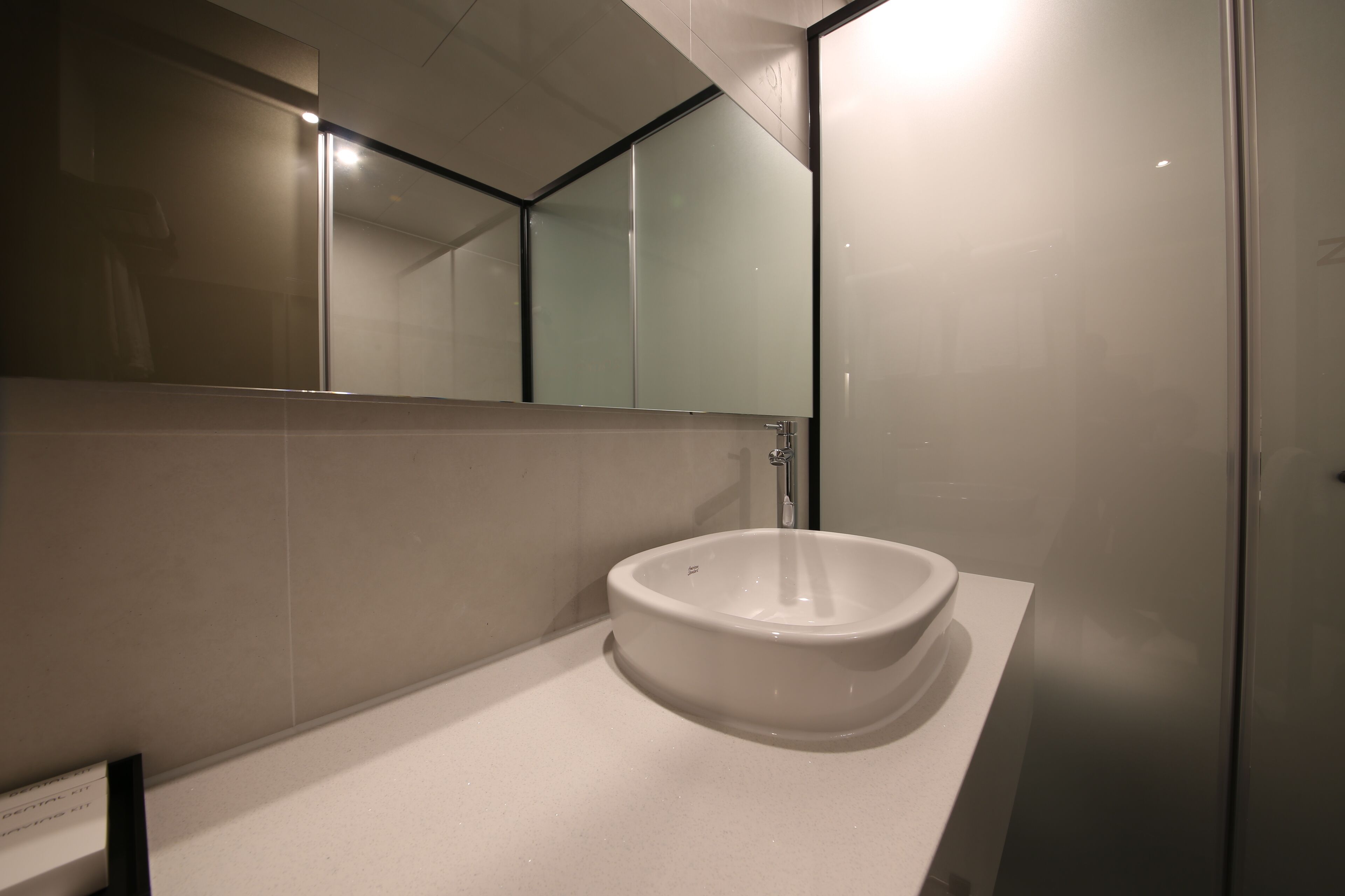 Ein modernes Badezimmer mit einem großen Spiegel, einem weißen Waschbecken und einer Dusche mit Glastrennwand.