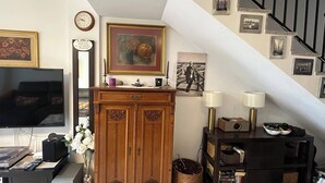 Un soggiorno con televisore, mobiletto in legno, opere d'arte incorniciate e una scala.