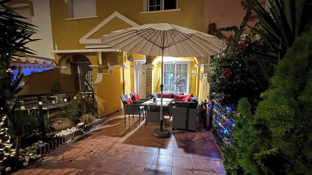 Un'area patio esterna con tavolo e sedie, una ventola e un ombrellone decorativo.