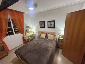 A bedroom with a bed, bedside table, dresser, vanity with mirror, and two wall art pieces.