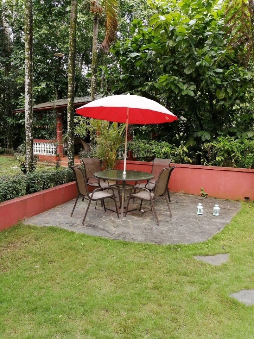 A patio with a round table and chairs, a red umbrella, and white lanterns.