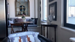 A cozy living room with a black leather sofa, a patterned throw blanket, a dining area with a wooden table and chairs, a large mirror, and a coffee shop sign above a window. - Uptown in Downtown (Anchorage)