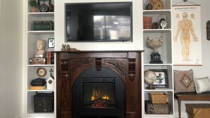 A living room with a fireplace, a mounted television, and shelves with various decorative items. - Uptown in Downtown (Anchorage)