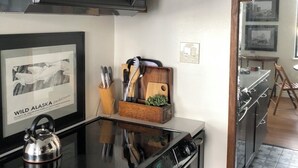 A kitchen with a black microwave, a framed picture of wild Alaska, and a wooden utensil holder. - Uptown in Downtown (Anchorage)