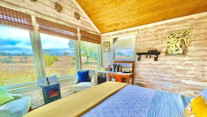 Een kamer met een bed, een stoel, een bureau en een groot raam met uitzicht op het landschap.