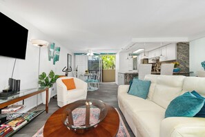 A modern living room with a white sofa, a glass coffee table, and a dining area with white chairs.
