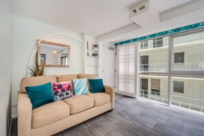 A modern living room with a beige sofa, teal cushions, a large mirror, and a sliding glass door leading to a balcony.