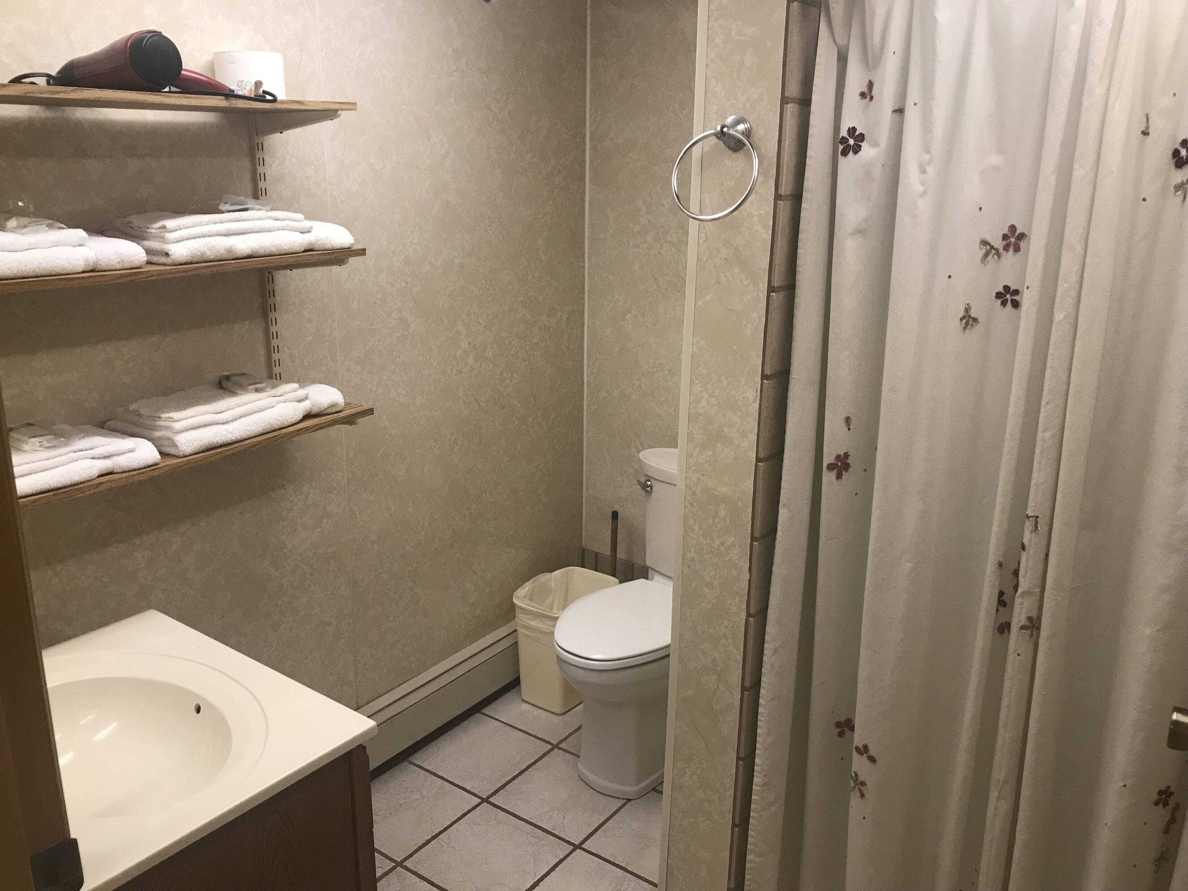 A bathroom with a toilet, a sink, and shelves with folded towels.
