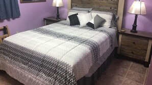 Un lit avec une couvre-lit à motifs géométriques, deux tables de chevet avec des lampes, une tête de lit en bois, un tableau encadré au mur et un rideau bleu.