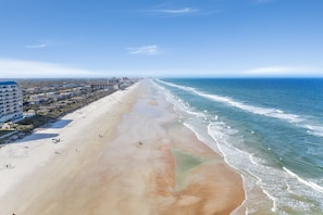 A long, sandy beach with a clear blue ocean, buildings along the shore, and a few people on the sand. - 🌊Wake Up to Ocean Views! Beachfront Balcony | Pool | Car Free Beach | Shore Villas (New Smyrna Beach)