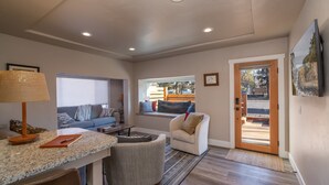 A modern living room with a sofa, a small table, a lamp, and a view of the outdoors through a window. - Tumalo House (Bend)