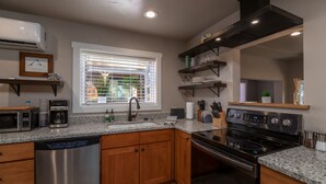 A modern kitchen with granite countertops, stainless steel appliances, wooden cabinets, and a built-in oven. - Tumalo House (Bend)