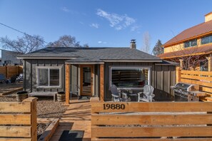 Una cabaña de madera con el número '19880' en la fachada, un patio con mobiliario exterior y una parrilla.