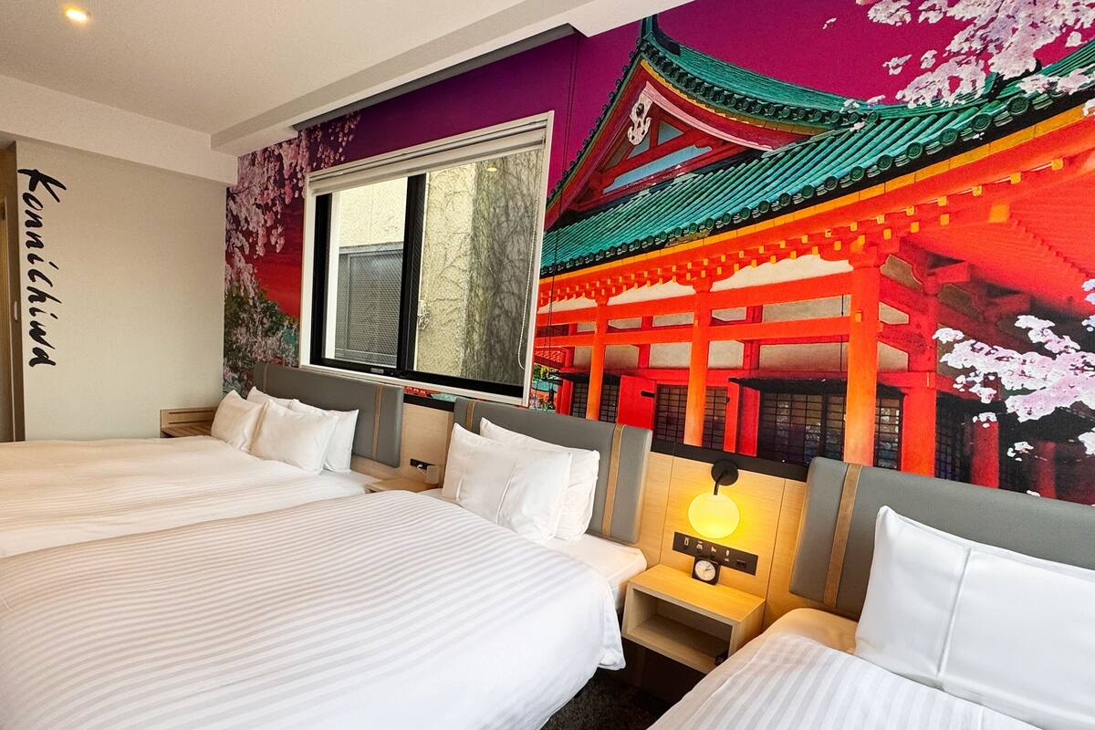 A hotel room with two beds, a large window, and a mural of a traditional building.